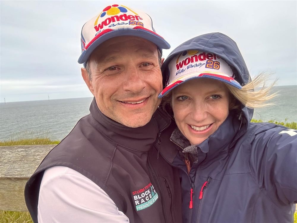 Bethany and Jeff in matching Wonder caps on a windy coastal bluff