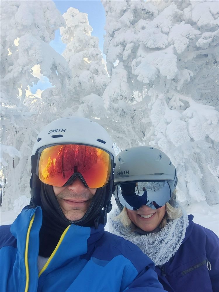 Bethany and Jeff in ski helmets in front of snow-covered trees